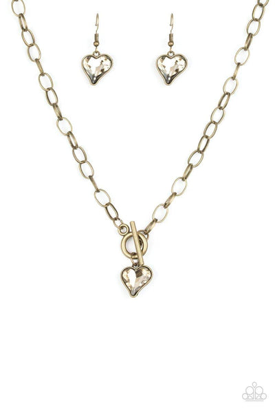 Cut into a whimsical heart shape, a glittery golden gem swings from the bottom of a glistening brass chain below the collar for a charming look. Features a toggle closure. Sold as one individual necklace. Includes one pair of matching earrings.  P2WH-BRXX-135XX