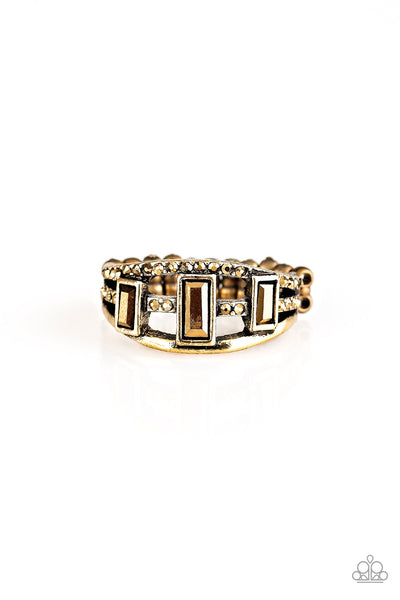Three aurum emerald-cut rhinestones are encrusted along three brass bands radiating with smooth surfaces and sections of glittery aurum rhinestones for an edgy fashion. Features a stretchy band for a flexible fit. Sold as one individual ring.  P4ED-BRXX-060XX