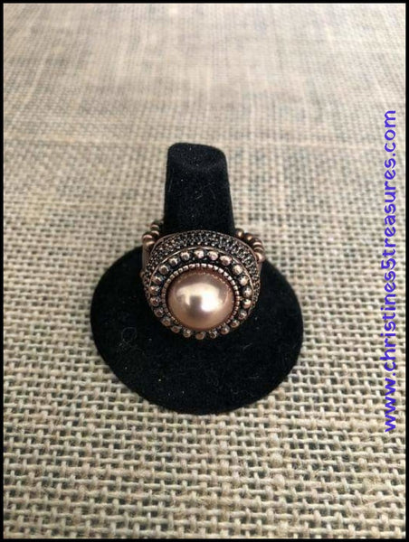 2018 October Fashion Fix Exclusive A pearly copper bead is pressed into the center of a stacked copper frame. Infused with classic copper studs and filigree detail, faceted copper studs spin around the pearly center, adding edgy shimmer to the dramatic centerpiece. Features a stretchy band for a flexible fit. Sold as one individual ring. P4RE-CPXX-086XX