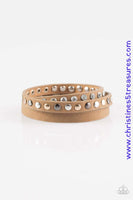 A skinny strip of brown leather is encrusted in sections of glittery white rhinestones and flat gold, gunmetal, and silver studs. The elongated band double wraps around the wrist for a fierce one-of-a-kind look. Features an adjustable snap closure. Sold as one individual bracelet.  P9DI-URBN-050XX