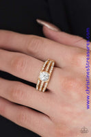 Encrusted in dainty white rhinestones, glistening gold bars layer across the finger, coalescing into a gorgeous band. A glittery white rhinestone is pressed into the center of the bands, creating a refined centerpiece. Features a dainty stretchy band for a flexible fit. Sold as one individual ring.  P4RE-GDXX-137XX