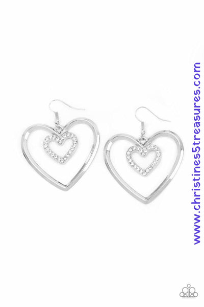 A dainty white rhinestone encrusted heart frame swings from the top of an oversized silver heart frame, creating a charming duo. Earring attaches to a standard fishhook fitting. Sold as one pair of earrings. P5RE-WTXX-445XX