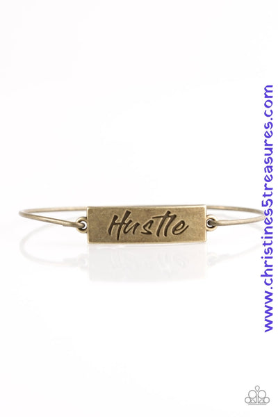 Engraved with the inspiring word "Hustle", a shimmery brass plate attaches to a skinny brass bar, creating a dainty bangle. Sold as one individual bracelet.  P9WD-BRXX-089XX